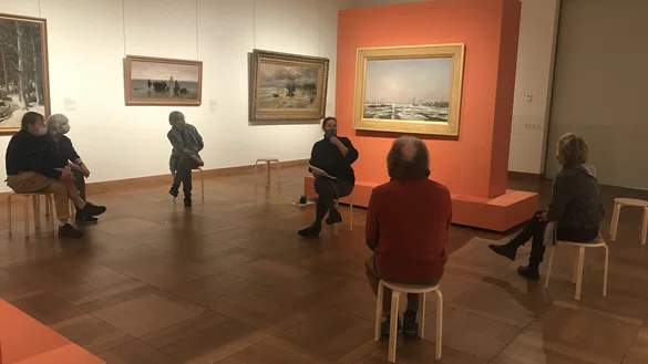 Bezoekers in een museumzaal zitten op krukken en nemen deel aan een workshop.