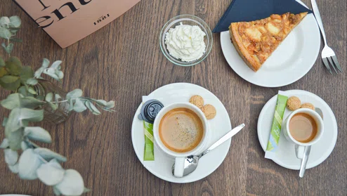 Een tafel met daarop twee kopjes koffie en appelgebak met slagroom