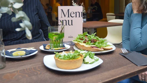 Een tafel in een cafe met twee personen. Op tafel staan broodjes