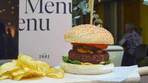 een burger op een plank met chips er naast, geserveerd op een tafel in een cafe