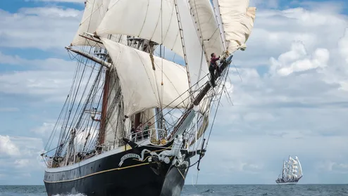 Een traditioneel houten zeilschip, de Morgenster, vaart over open water met meerdere witte zeilen vol in de wind. Het schip heeft een hoge mast, tuiga