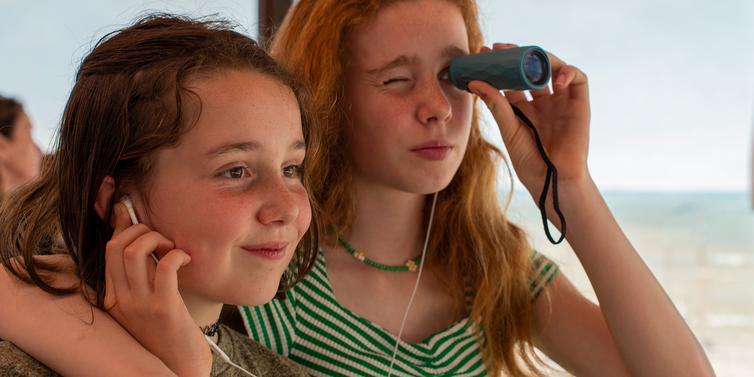 Zusjes kijken met een verrekijker het panorama terwijl ze samen via oortjes naar een audiotour luisteren.