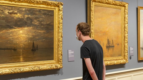 Bezoeker met een mondkapje op kijkt naar een van de kunstwerken op zaal.
