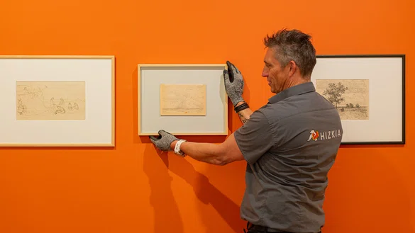 Een arthandeler hangt een schets op tussen twee werken aan de muur