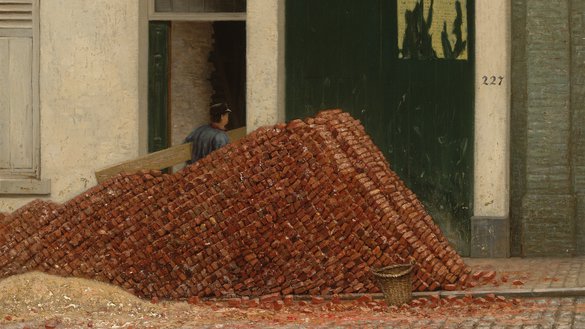 Een stapel bakstenen ligt op straat en daarachter loopt een werkman die een plank draagt een huis binnen.