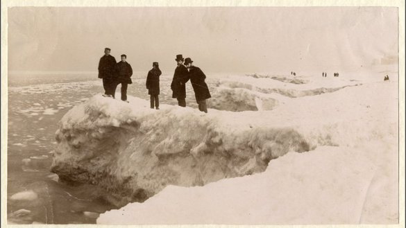Vijf personen staan op een ijsschots van de deels bevroren Noordzee bij Scheveningen.
