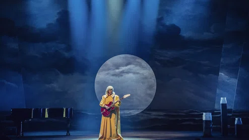 cabaretier Claudia de Breij speelt gitaar op het podium in een gele jurk