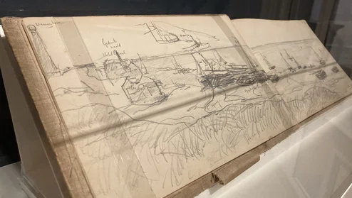 opengeslagen schetsboek met potloodtekening van boten op het strand